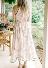 Back view of Model wearing a pale pink midi with a floral design, green piping and elastic waist.