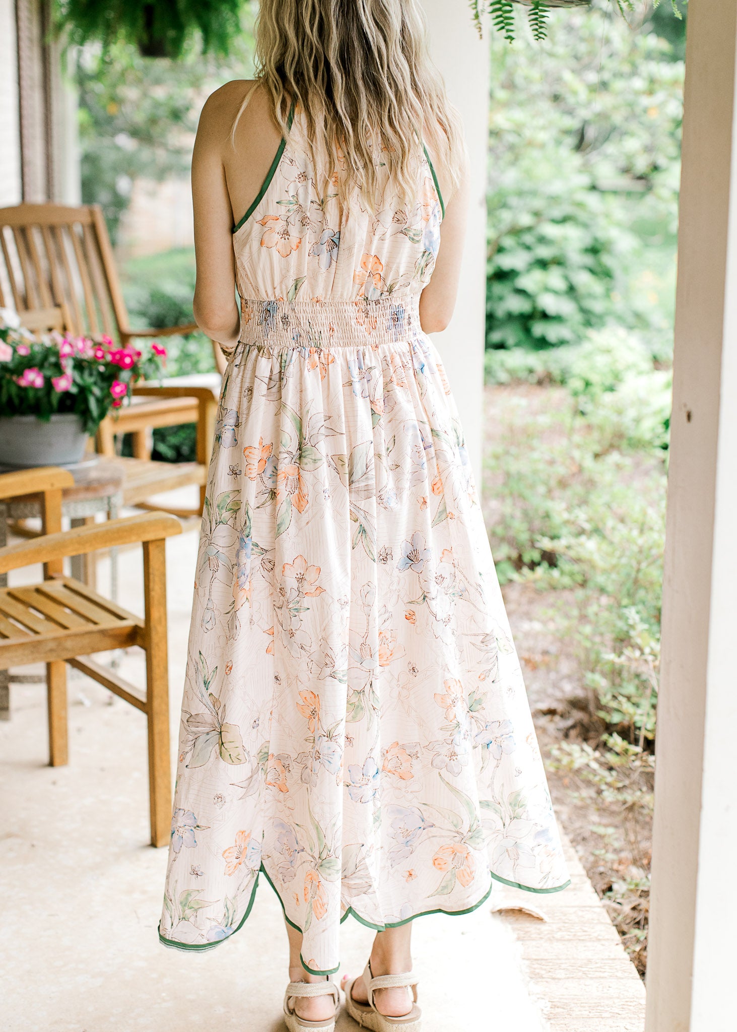 Back view of Model wearing a pale pink midi with a floral design, green piping and elastic waist.