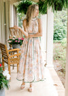 Model wearing a sleeveless pale pink midi with a floral design, green piping, and elastic waist.