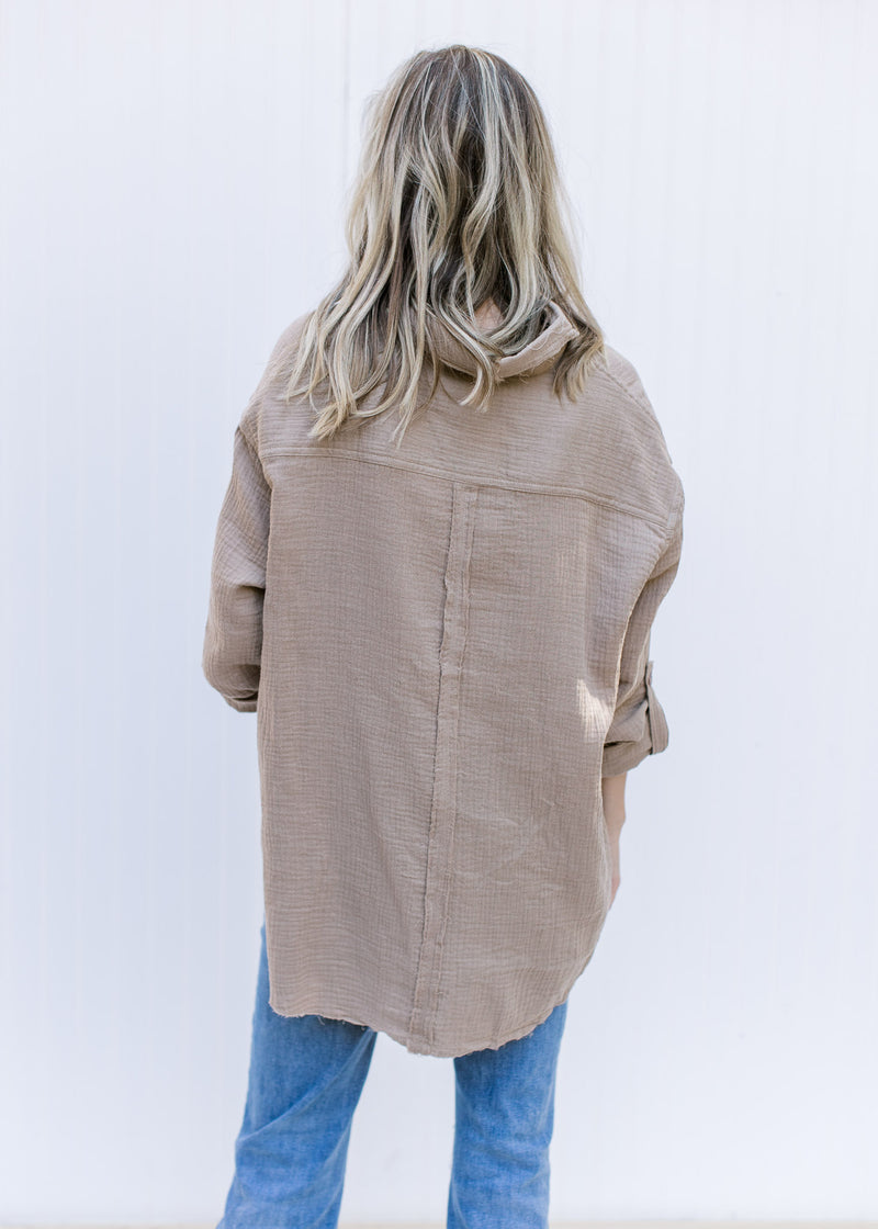 Back view of a taupe button up top with a raw hemline and a cotton gauze material with jeans. 