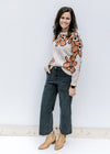 Model wearing black jeans with a taupe sweater with a round neck and rust flowers outlined in black.