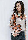 Model wearing a taupe long sleeve sweater with a round neck and rust flowers outlined in black. 