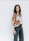 Model wearing a taupe long sleeve sweater with rust flowers outlined in black tucked in black jeans.