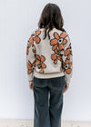Back view of Model wearing a taupe sweater with a round neck and rust flowers outlined in black. 