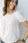 Close up of smocked yolk and bubble short sleeves on a cream top with a square neck.