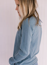 Detail view of ribbing down the long sleeve of a light blue sweater with a crew neckline. 