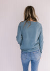 Back view of Model wearing a light blue sweater with a crew neck and long sleeves.