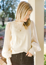 Model wearing an ivory top with shimmer long sleeves, ribbed bodice and a polyester material. 