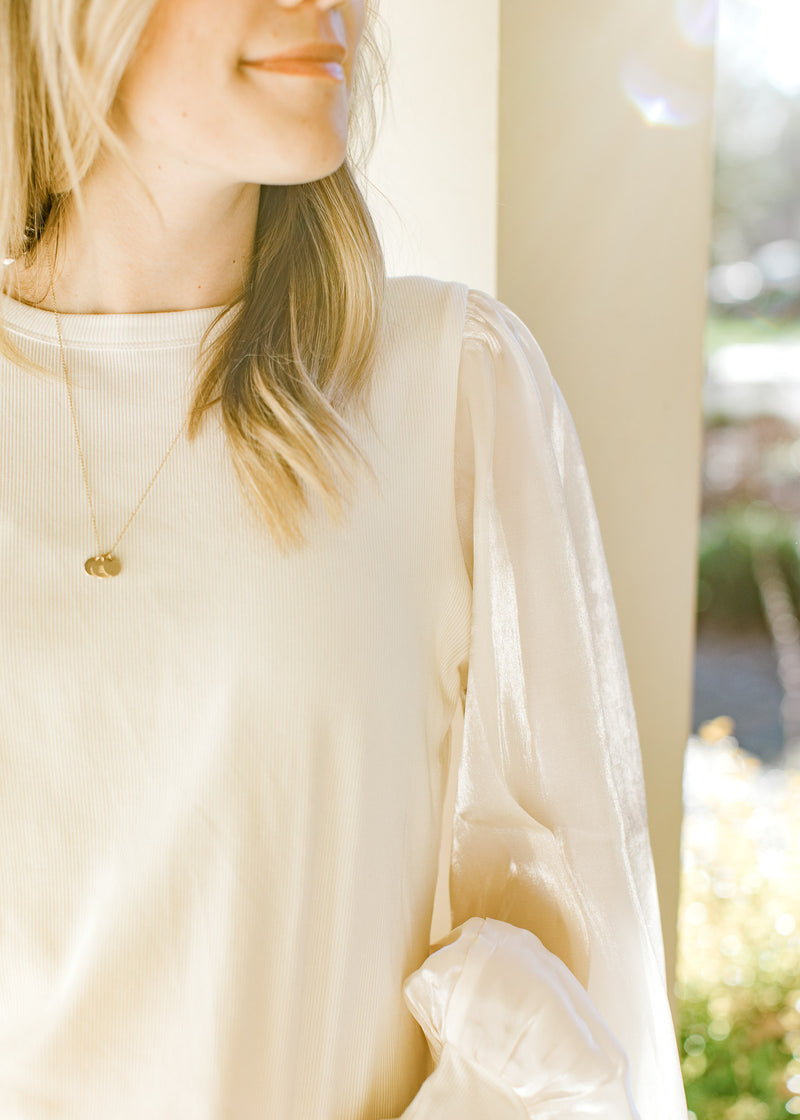 Close up of shimmer long sleeves on an ivory top with a ribbed bodice and a polyester material. 
