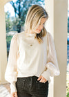 Model wearing an ivory top with shimmer long sleeves, ribbed bodice and a round neck. 