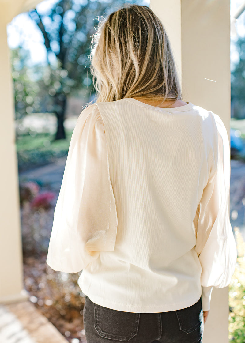 Back view of Model wearing an ivory top with shimmer long sleeves and a ribbed bodice.