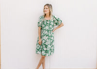 Model wearing a bright green knee length dress with cream floral, tiers and bubble short sleeves.