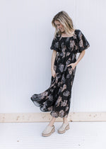 Model wearing mules with a black maxi with tan and gray flowers, short sleeves and a square neck.