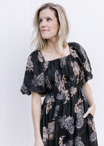Close up of square neck and bubble short sleeves on a black maxi with a gray and tan flowers.  