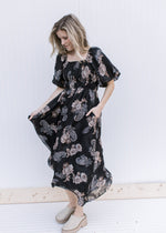 Model twirling in a black maxi with tan and gray flowers, bubble short sleeves and a square neck.