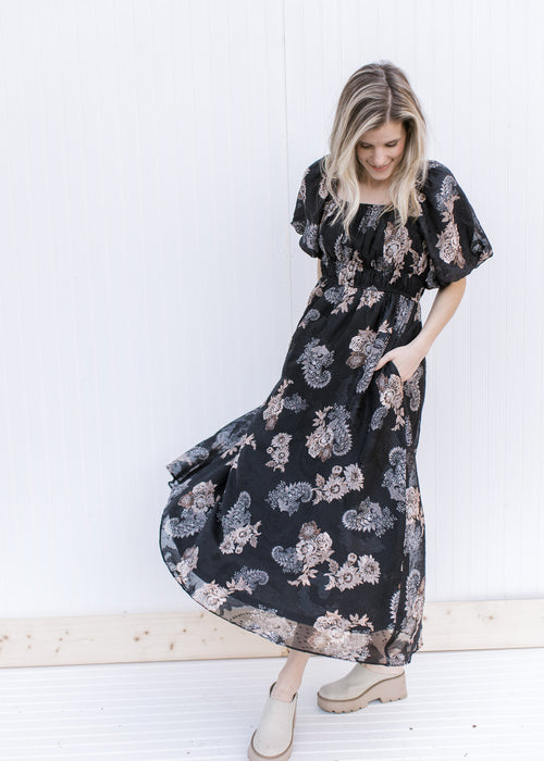 Model wearing a black maxi with tan and gray flowers, bubble short sleeves and a square neckline. 
