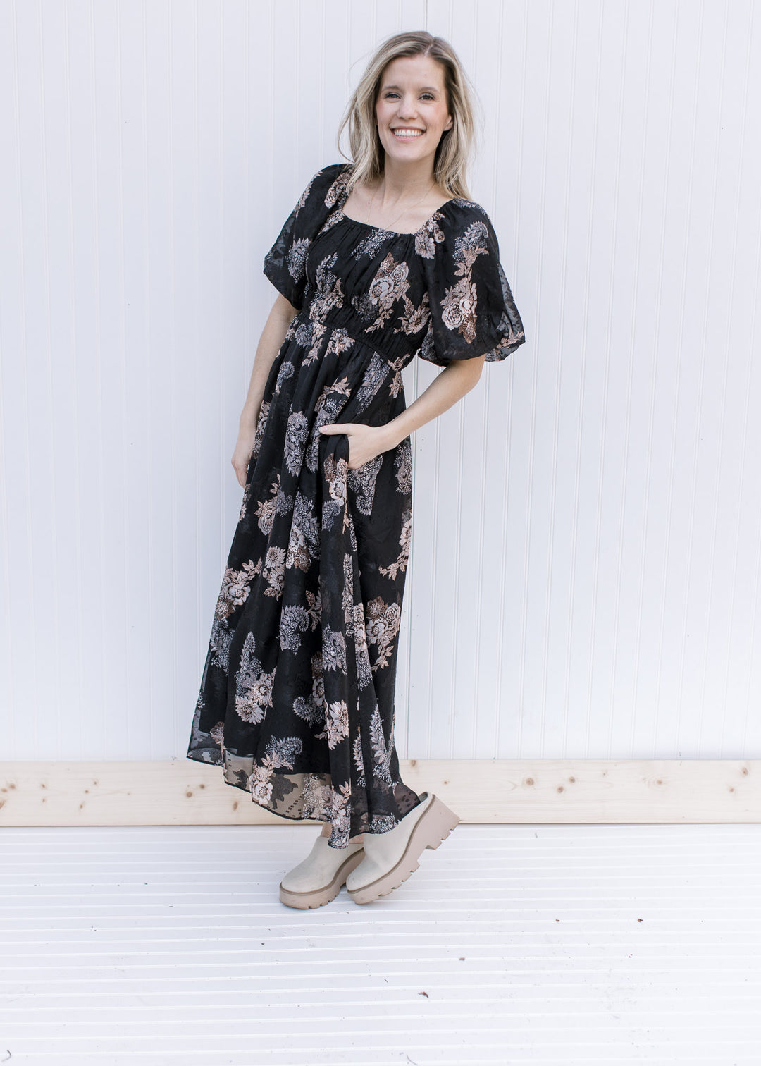 Model wearing a black maxi with tan and gray flowers, bubble short sleeves and pockets.