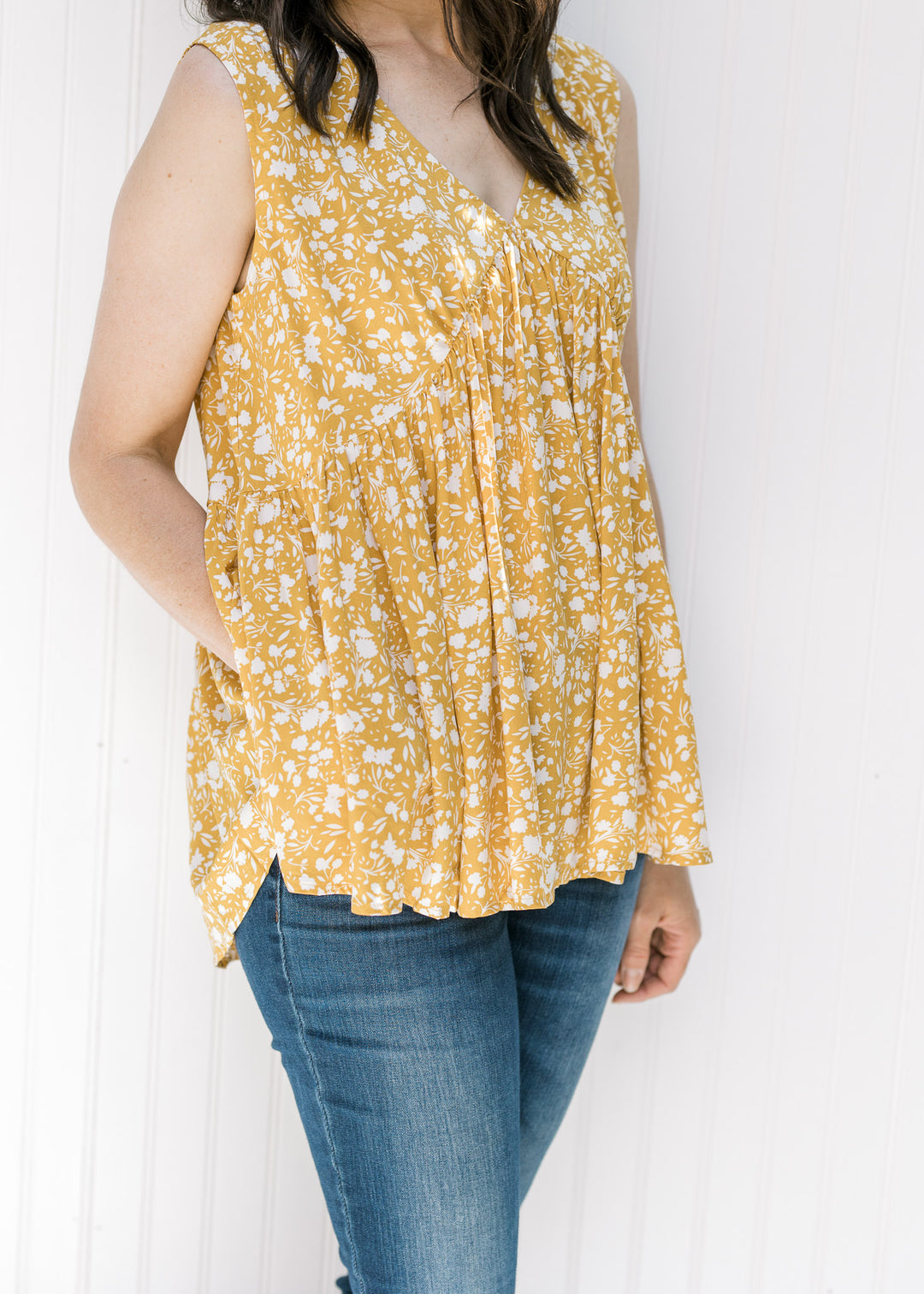 Close up view of Model wearing a sleeveless mustard yellow v-neck top with a cream floral pattern. 