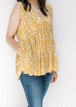 Close up view of Model wearing a sleeveless mustard yellow v-neck top with a cream floral pattern. 