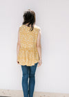 Back view of Model wearing a sleeveless mustard yellow v-neck top with a cream floral pattern. 