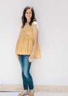 Model wearing jeans with a sleeveless mustard yellow v-neck top with a cream floral pattern. 