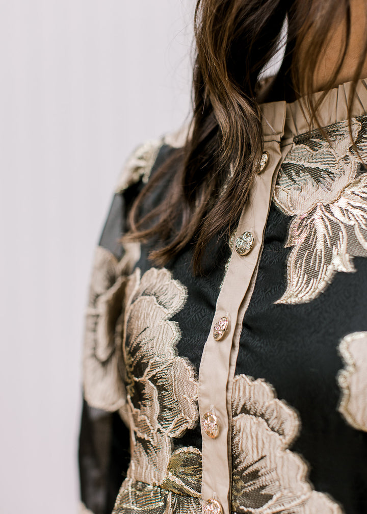 Close up of gold buttons along the placket of a black top with golden flowers and a mock neck.