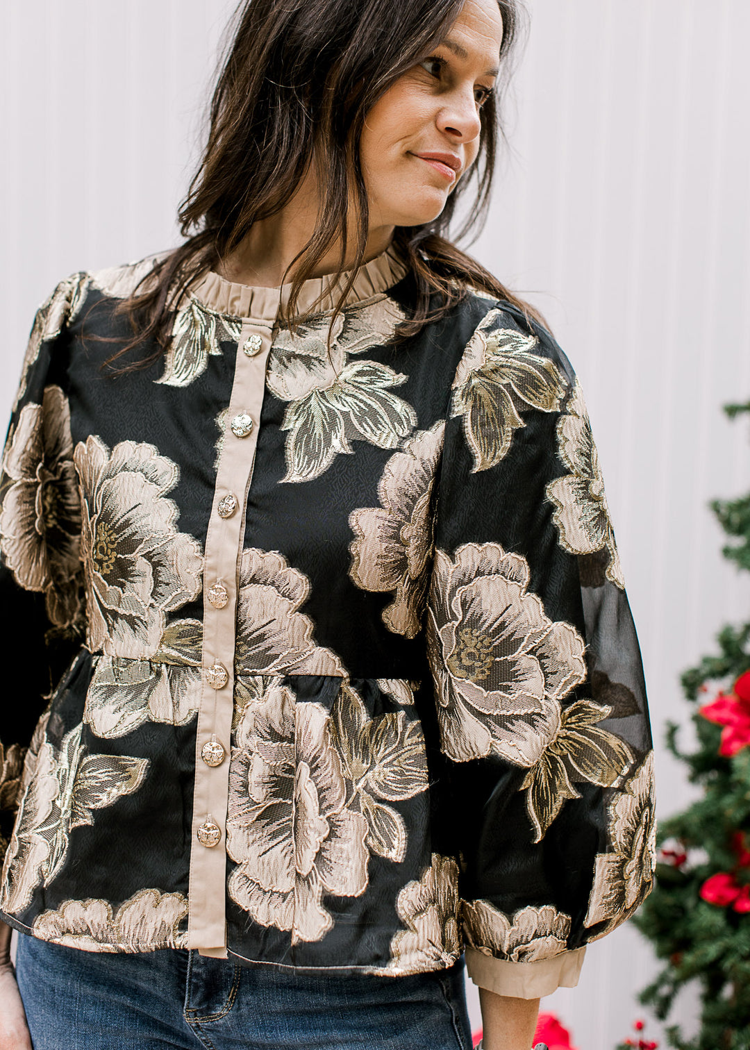 Model wearing a black top with gold floral, button front, bubble long sleeves and a mock neck. 