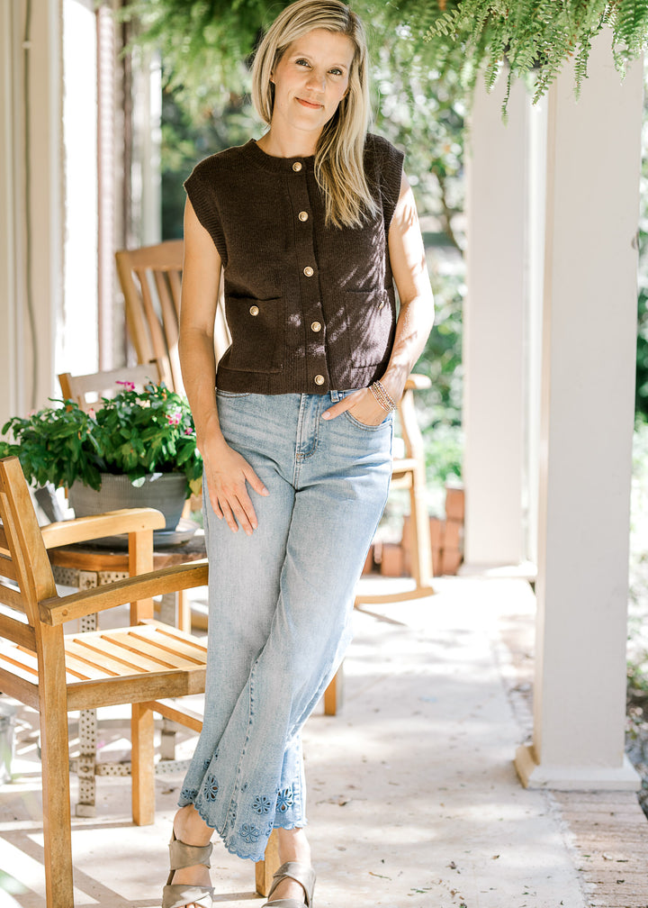 Model wearing jeans and a mocha sleeveless top with patch pockets and gold button front. 