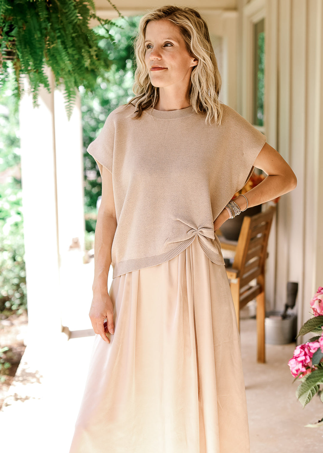 Model wearing a soft gold knit sweater with capped sleeves, round neck and gathered detail at hem.