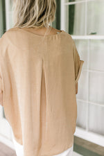 Back view of model wearing a gold textured top with a round neck and cuffed short sleeves. 