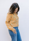 Model wearing a long sleeve mustard button up sweater with yellow and green stitched flowers. 