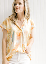Model wearing a golden yellow v-neck top with a watercolor floral design, short sleeves and a collar
