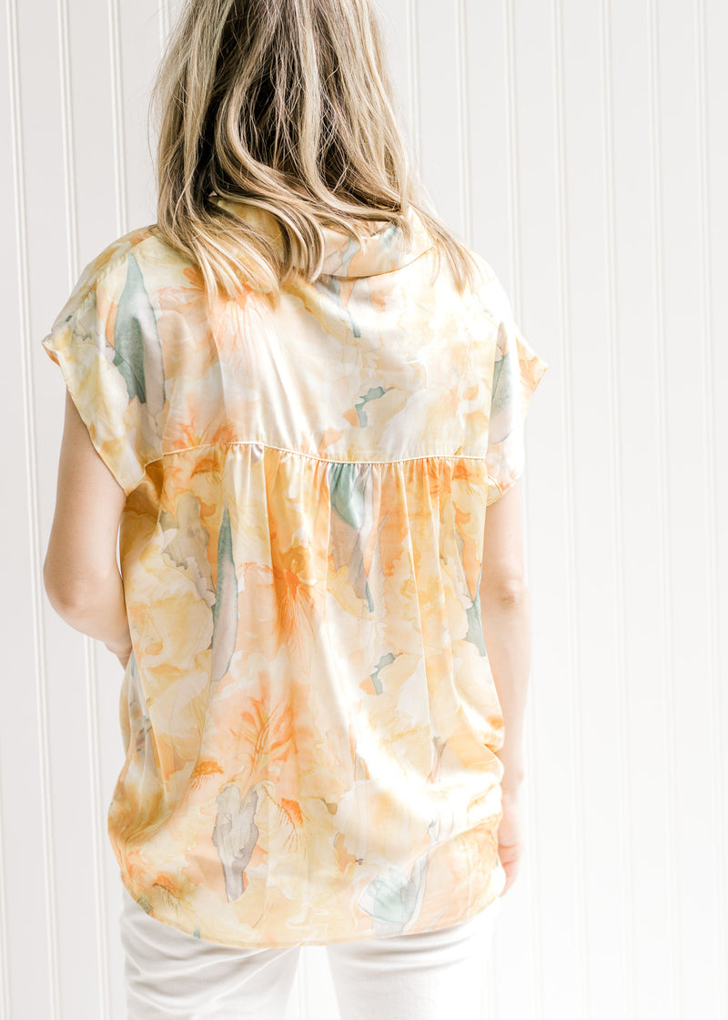 Back view of Model wearing a golden yellow v-neck top with a watercolor floral design. 