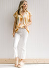Model wearing white jeans with a golden yellow short sleeve top with a watercolor floral design. 