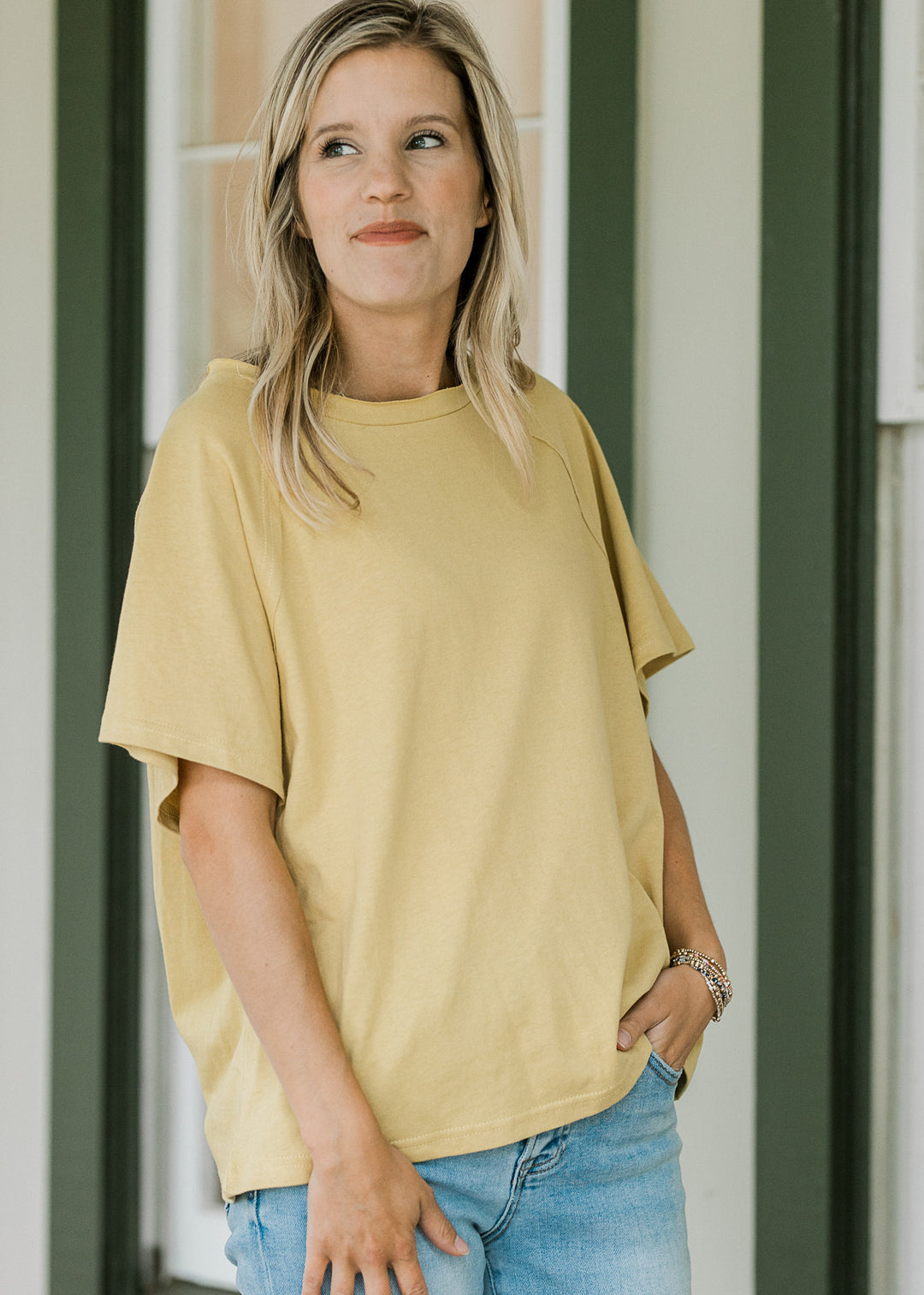 Model wearing a golden yellow tee with round neck, seem in back, short sleeves and a loose fit. 