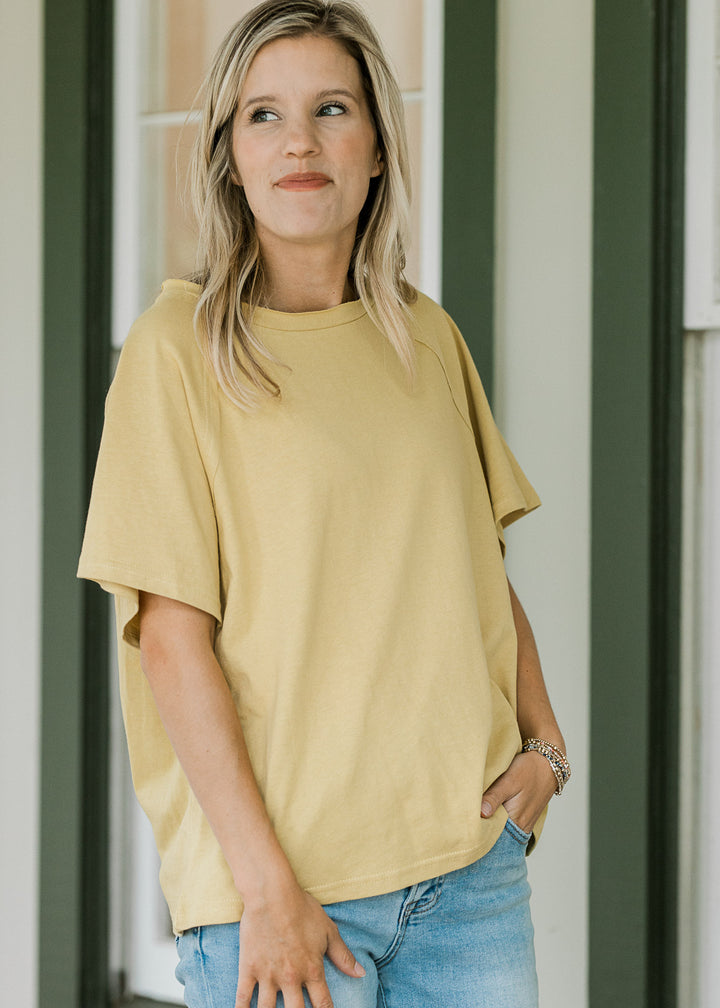 Model wearing a golden yellow tee with round neck, seem in back, short sleeves and a loose fit. 