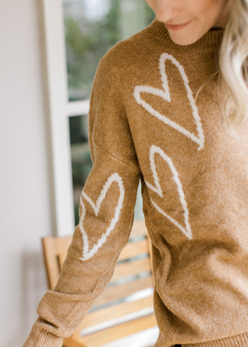 Close up of cream hearts on a golden sweater with long sleeves, a round neck and classic styling. 