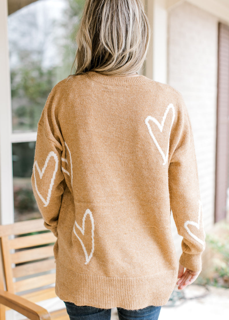 Back view of Model wearing a golden sweater with cream heart pattern and long sleeves.