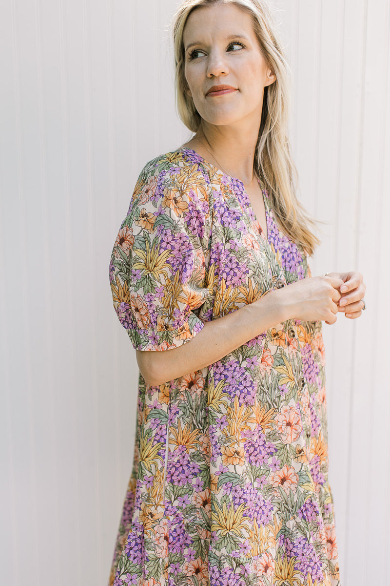 Model wearing a cream dress with multi colored floral, v-neck and short sleeves.