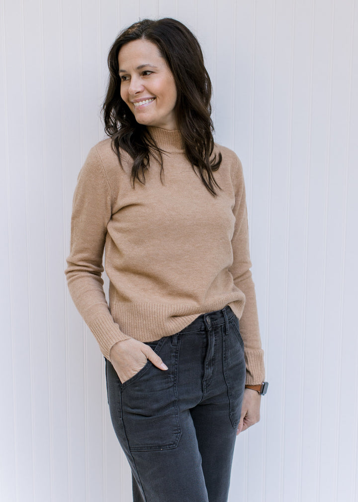 Model wearing a classic camel colored top with a mocked neckline and long sleeves. 