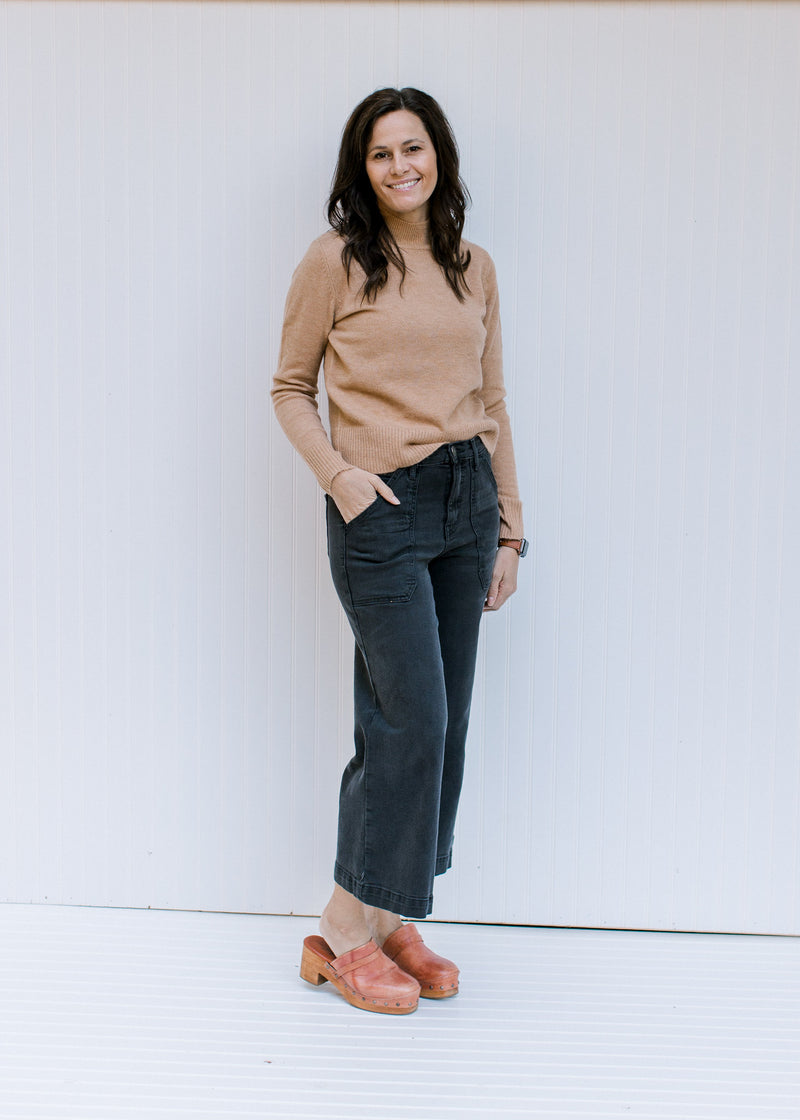Model wearing jeans and mules with a camel colored top with a mocked neckline and long sleeves. 