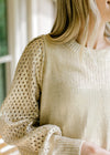 Close up of eyelets on the long sleeve of a golden shimmer sweater with a round neck. 