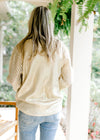 Back view of Model wearing a golden shimmer sweater with eyelets on the long sleeves.