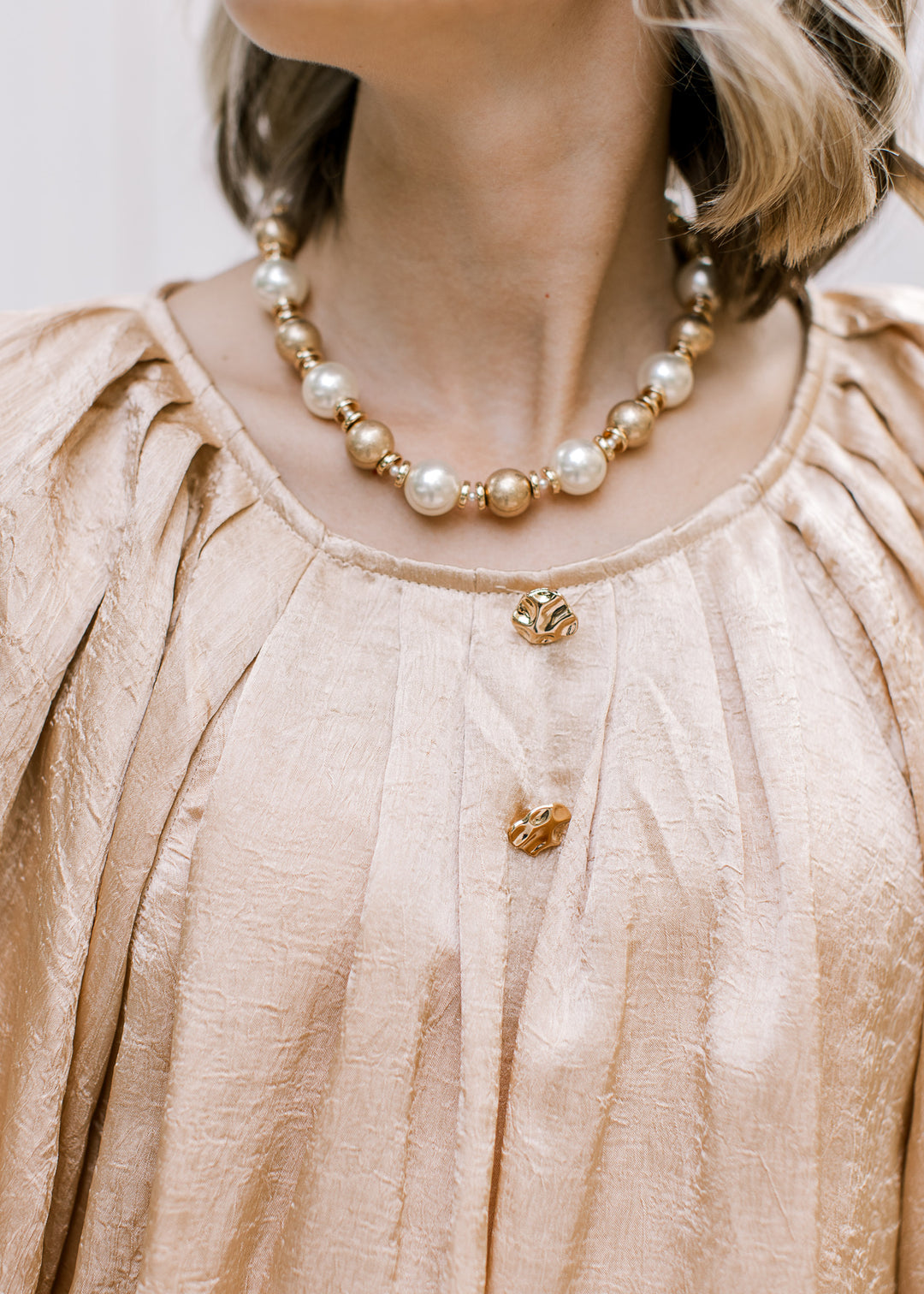 Close-up of Golden Shimmer Top showing pleated round neckline, two hammered gold buttons and lustrous fabric.