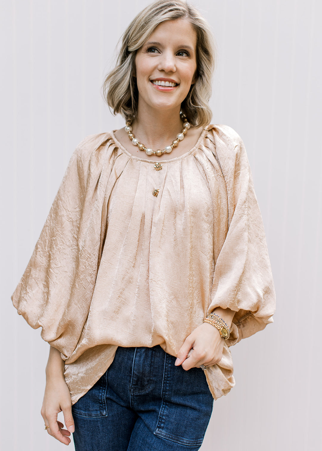 Golden Shimmer Top tucked into dark jeans, showing pleated round neckline, gold buttons and voluminous bubble sleeves.