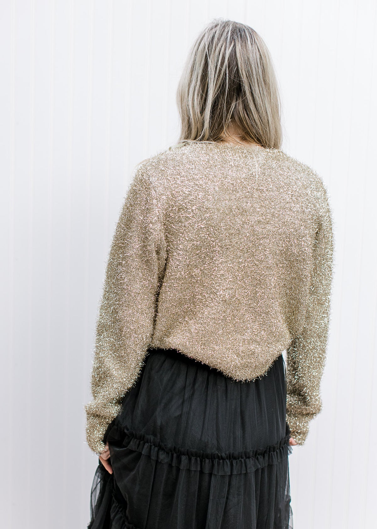 Back view of  Model wearing a gold sweater with a tinsel material, round neck and long sleeves. 
