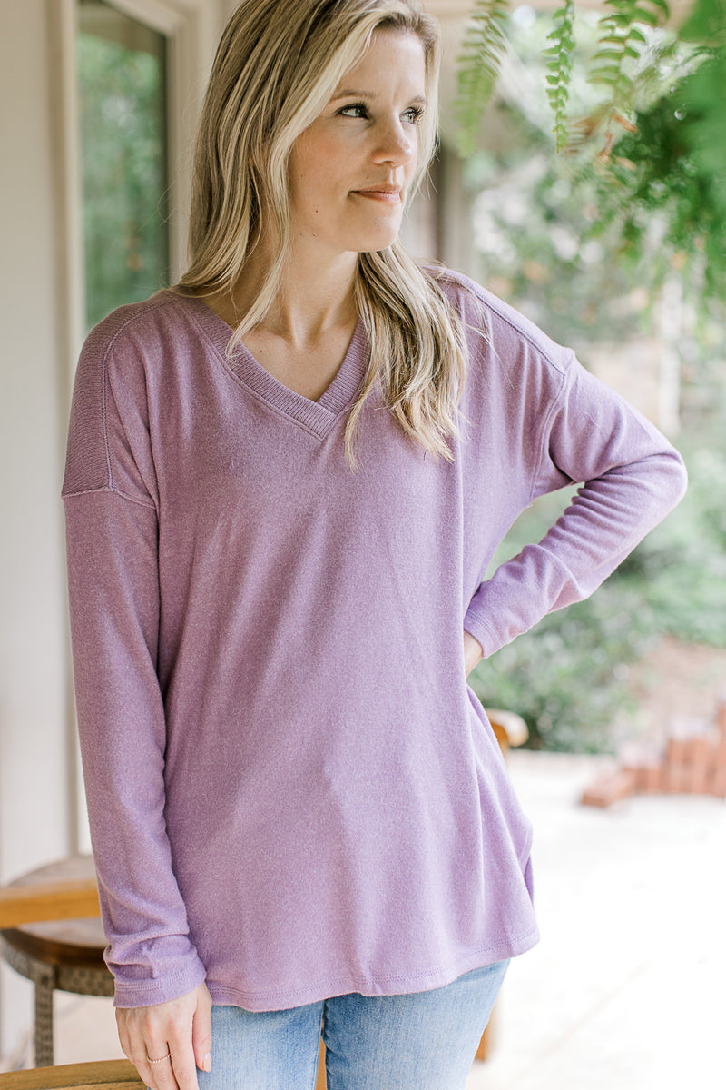 Model wearing a lavender sweater with  a ribbed v-neck and long sleeves. 