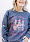 Model wearing a charcoal sweatshirt with 3 nutcrackers, pink text and long sleeves. 