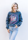 Model wearing a charcoal long sleeve sweatshirt with 3 nutcrackers, pink text and round neck.