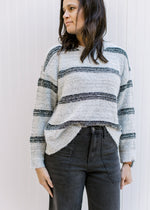 Model wearing jeans with a cozy gray sweater with black stripes, long sleeves and a round neck. 